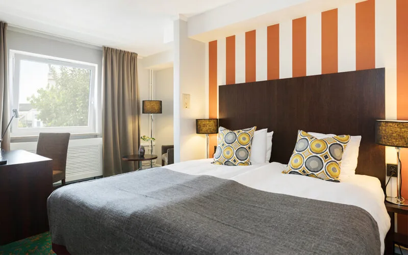 Hotellrum med dubbelsäng, orange randig fondvägg och sittgrupp vid fönster.