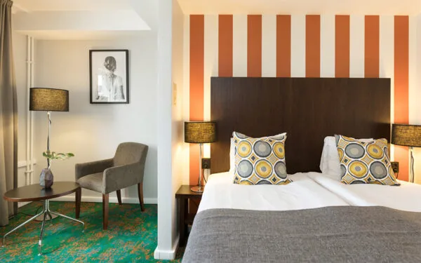 Hotellrum med dubbelsäng, orange randig fondvägg och skrivbord med stol