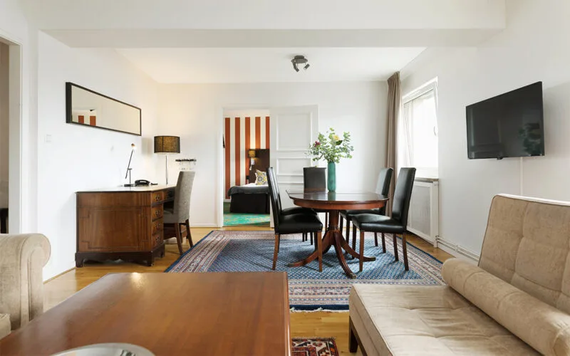 Vardagsrumsdel i hotellsvit med soffgrupp, soffbord, matbord och målning på väggen