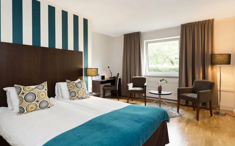 Hotellrum med dubbelsäng, turkost överkast och randig fondvägg