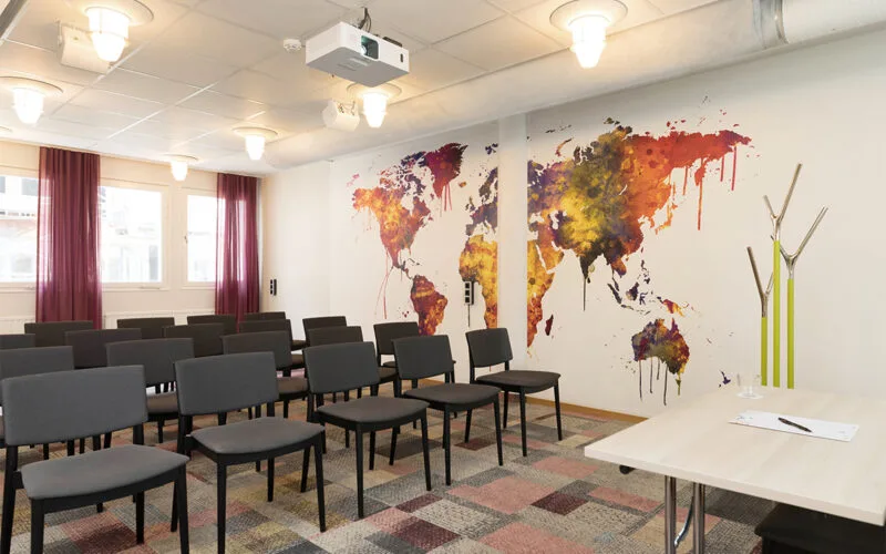 Konferensrum med svarta stolar, projektor i taket och en färgglad världskarta som väggmålning