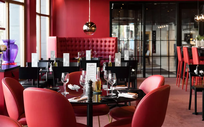 Restaurangmiljö med dukade bord och röda stolar.