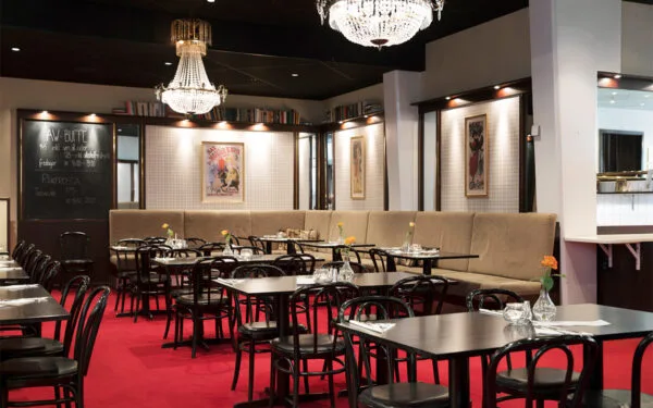 Elegant restauranginteriör med röda heltäckningsmattor, svarta bord och stolar, kristallkronor i taket och tavlor på väggarna