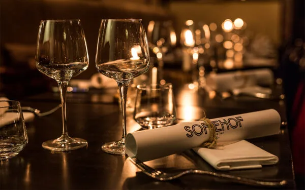 Närbild av dukat bord med glas, servett och varm belysning.