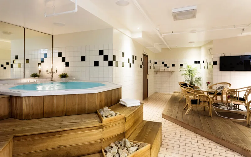 Relaxavdelning med jacuzzi, vita kakelväggar och trädetaljer.