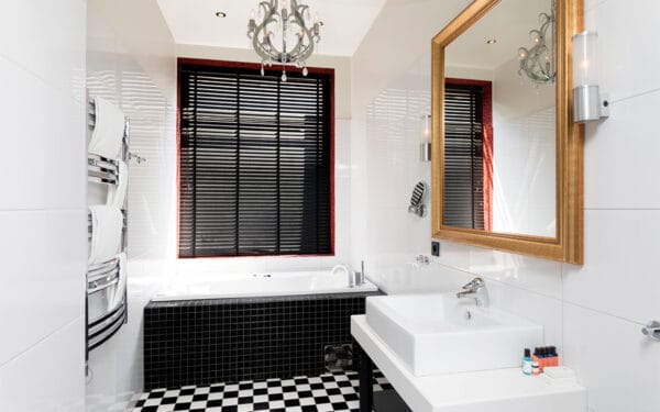 Badrum med svartvit klinker, vit inredning och stort fönster med persienner.