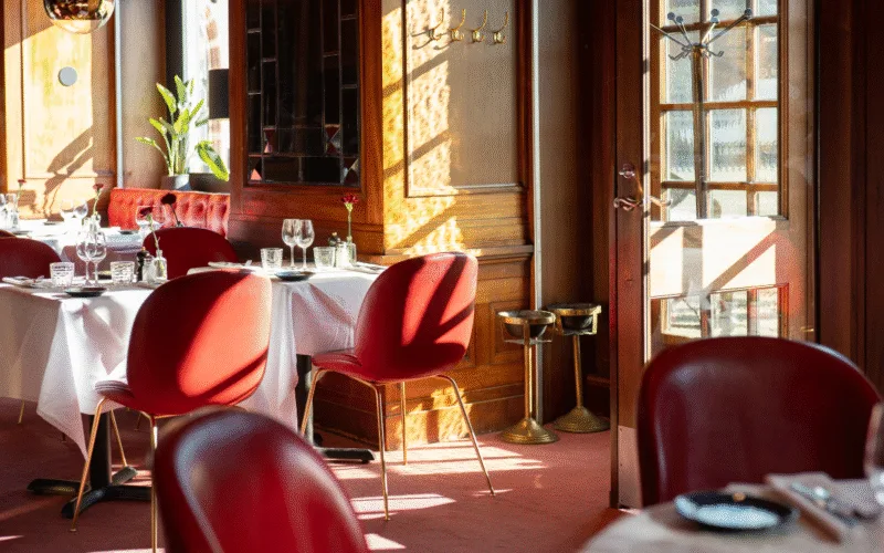 Dukat runt bord med vit duk, glas och serviser, omgivna av röda stolar i en elegant restaurangmiljö