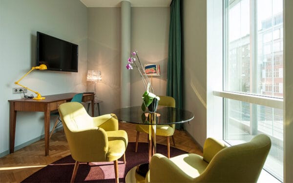 Sittgrupp med tre fåtöljer, runt bord med orkidé, skrivbord och TV på väggen.