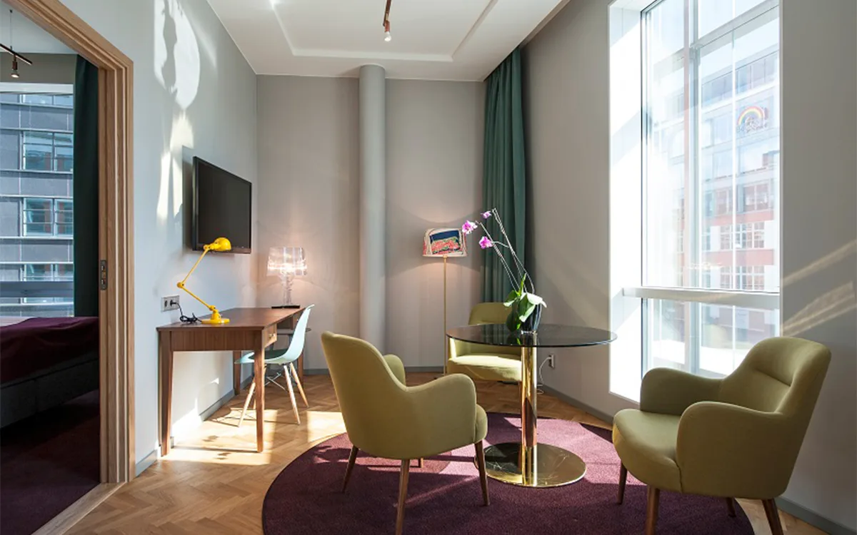 Ljus sittgrupp med runda bord, gröna fåtöljer och stora fönster.