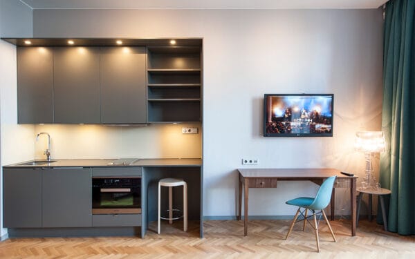 Pentry i grått med spis och ugn, barpall, skrivbord med stol och TV på väggen.