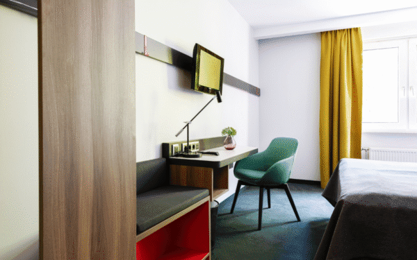 Abstellfläche, Schreibtisch, Sitzgelegenheit und Fernseher des Doppelzimmers Plus.