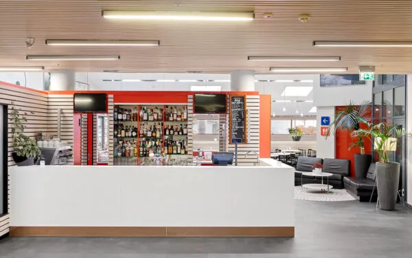 Hotel bar with a white bar, shelves with bottles, TV screens, and seating in the background.