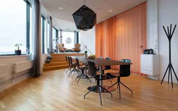 Modernt mötesrum i penthousevåning med långbord, svarta stolar, stora fönster med utsikt, teleskop och loungehörna i bakgrunden.