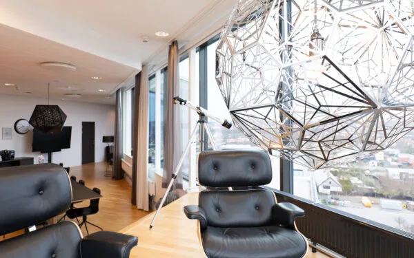 Lounge med läderfåtöljer, taklampa och teleskop vid fönster.