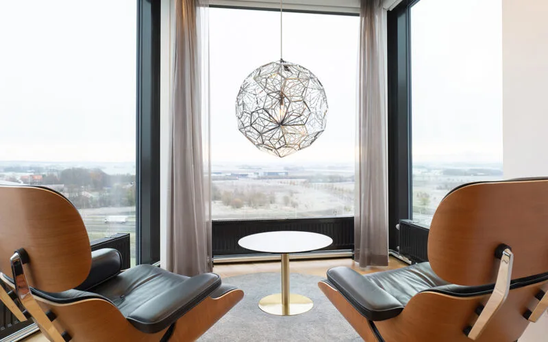 Sittgrupp med fåtöljer, bord och utsikt genom panoramafönster.