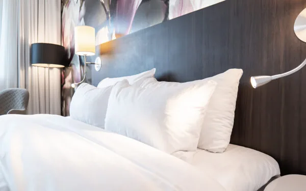 Bäddad dubbelsäng med vita kuddar och täcke, mörk träpanel som sänggavel och dekorativ tapet med magnoliablommor i bakgrunden.