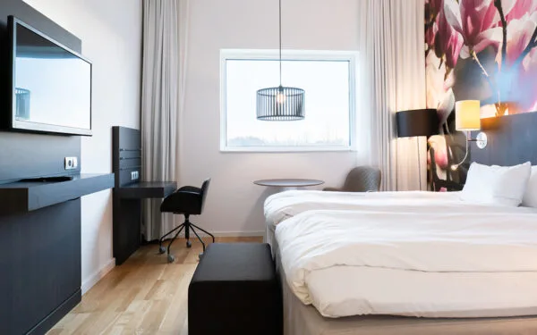 Hotellrum med två bäddar, skrivbord, platt-TV och stort fönster som släpper in naturligt ljus.