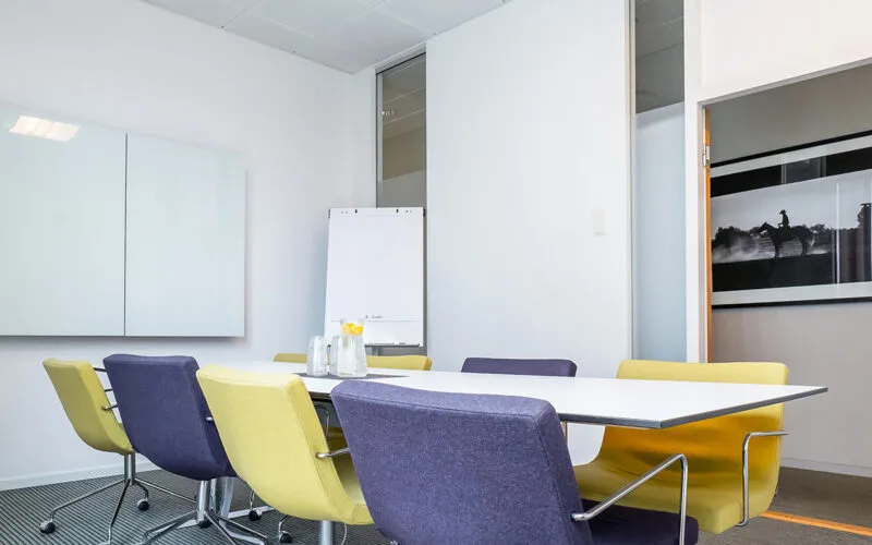 Litet mötesrum med stolar runt ett bord, blädderblock vid väggen och glas med vatten och citron på bordet.
