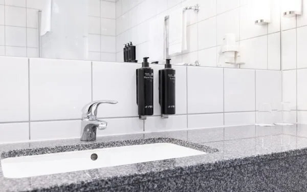 Badrum med vitkaklade väggar, granitbänk och dispenser för handtvål och lotion vid spegeln.