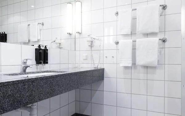 Badrum med vitkaklade väggar, handfat med granitbänk, två vägghängda tvålpumpar, hårtork samt flera upphängda handdukar.