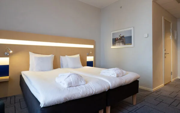 Hotellrum med dubbelsäng, sänggavel med inbyggd belysning och två läslampor och två morgonrockar på sängen.