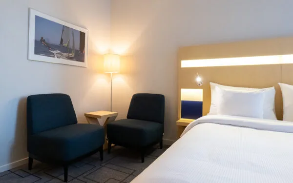 Hotellrum med dubbelsäng, två fåtöljer vid ett litet bord, golvlampa och tavla på väggen.