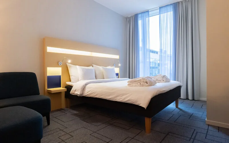 Hotellrum med dubbelsäng, sittplats och stort fönster.