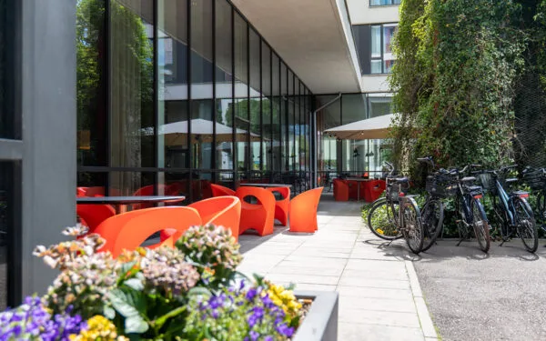 Hotellterrass med uteservering, färgglada stolar, blommor och parkerade cyklar.