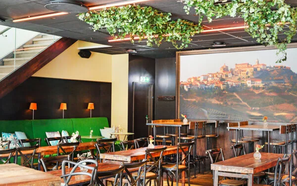 Restaurangmiljö med träbord, grön soffa och stor väggbild.