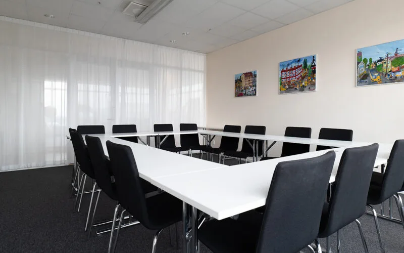 Konferensrum med vita bord, svarta stolar och tavlor på väggen.