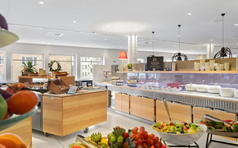 Frukostbuffé i hotellrestaurang med serveringsstationer, färska råvaror och sittplatser vid fönstren.