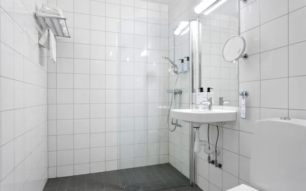 Modernt hotellbadrum med dusch, handfat och toalett.