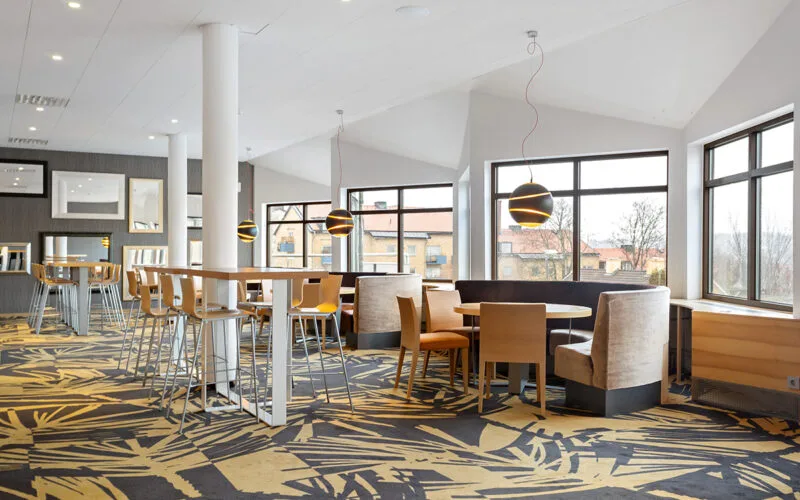 Mötesrum med stora fönster, runda bord, sittbås och höga barstolar.