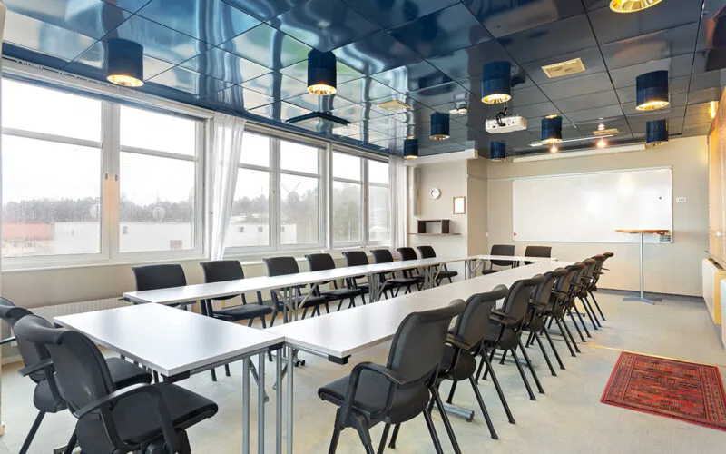 Konferensrum med U-formad möblering, svarta stolar, whiteboard och stora fönster.