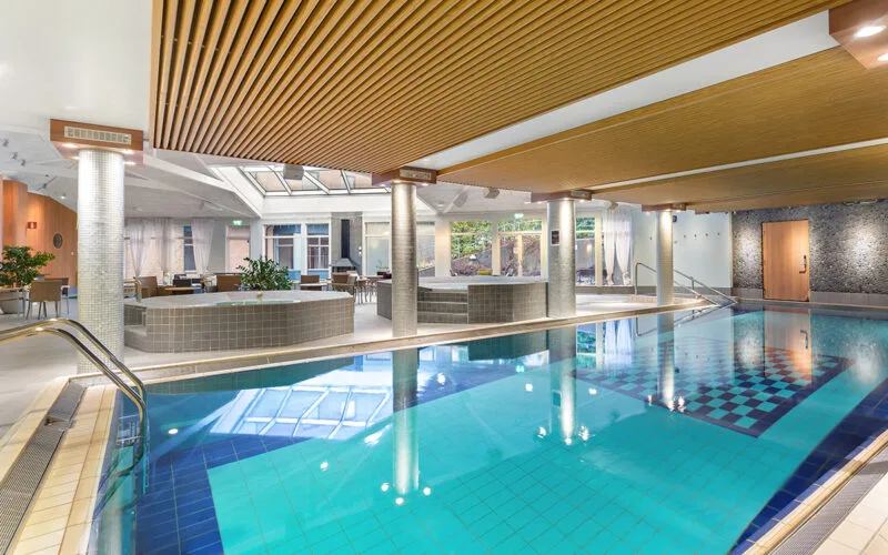 Inomhuspool, omgiven av pelare, loungeytor och stora fönster som släpper in ljus.