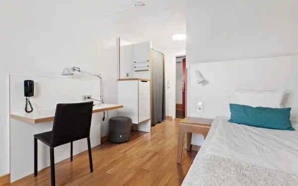 Enkelrum med enkelsäng, skrivbord och stol samt garderob.