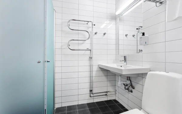 Modernt badrum med vitt kakel, dusch med frostat glas, handfat och toalett.