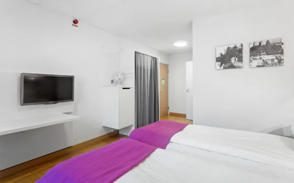 Dubbelrum med två bäddar, väggmonterad TV och svartvita tavlor på väggen.