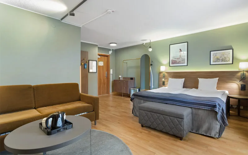 Hotellrum med dubbelsäng, soffa, soffbord och modern inredning i mjuka färger.
