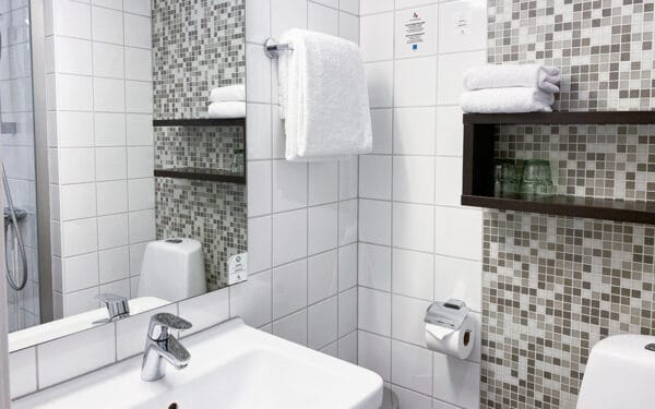 Hotellbadrum med vitt kakel, handfat och handdukar.