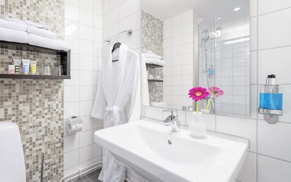 Hotellbadrum med vitt kakel, handfat och spegel.