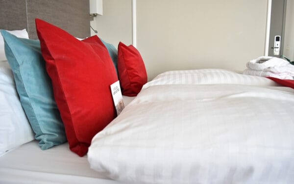 Närbild på hotellsäng med krispiga vita lakan och röda kuddar.