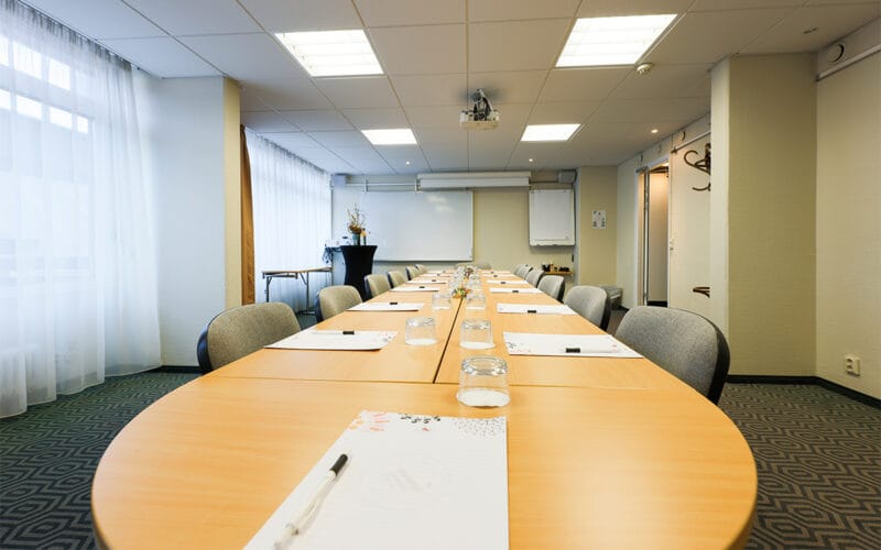 Mötesrum med långbord, stolar och dukade block för möte