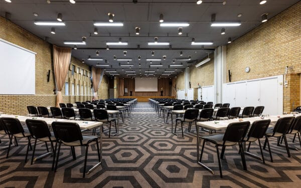 Större möteslokal med uppställda bord och stolar i klassrumsstil.