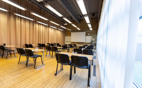 Större möteslokal med uppställda bord och stolar i klassrumsstil.