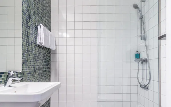 Badrum med dusch, handfat och kaklade väggar.