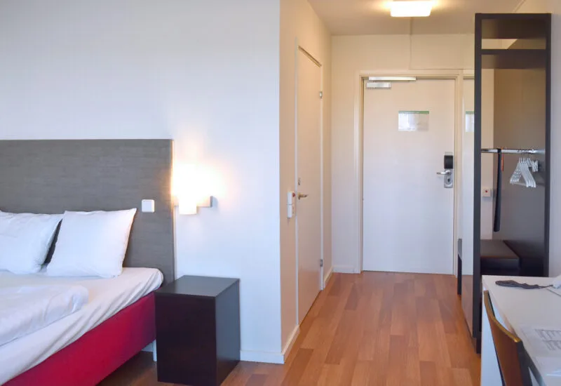 Hotellrum med säng, nattduksbord och garderob med galgar.