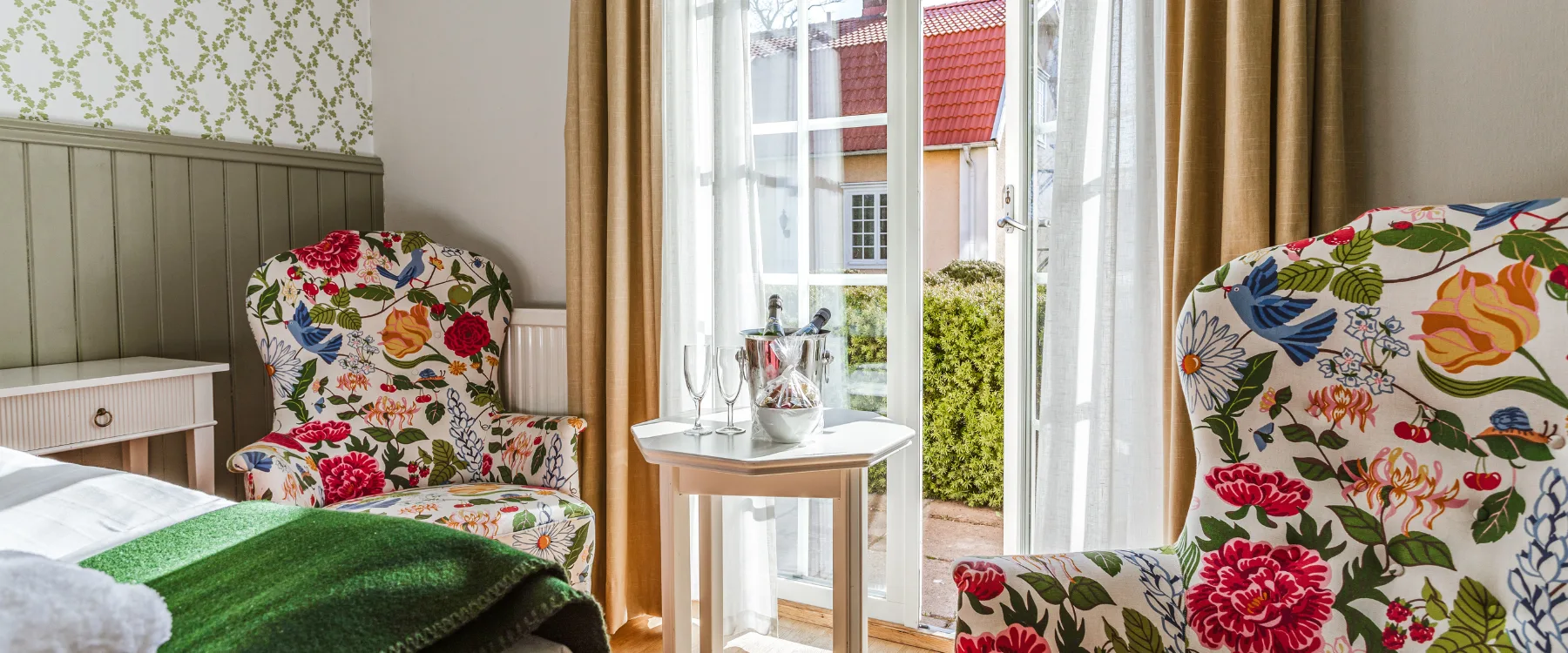 Hotellrum med blommiga fåtöljer, franska dörrar och utsikt mot innergård