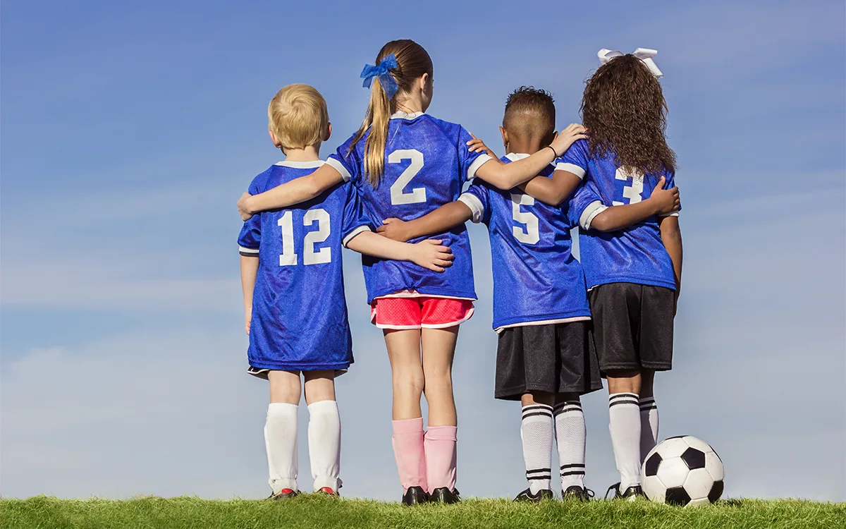 Four children in football shirts with a ball.