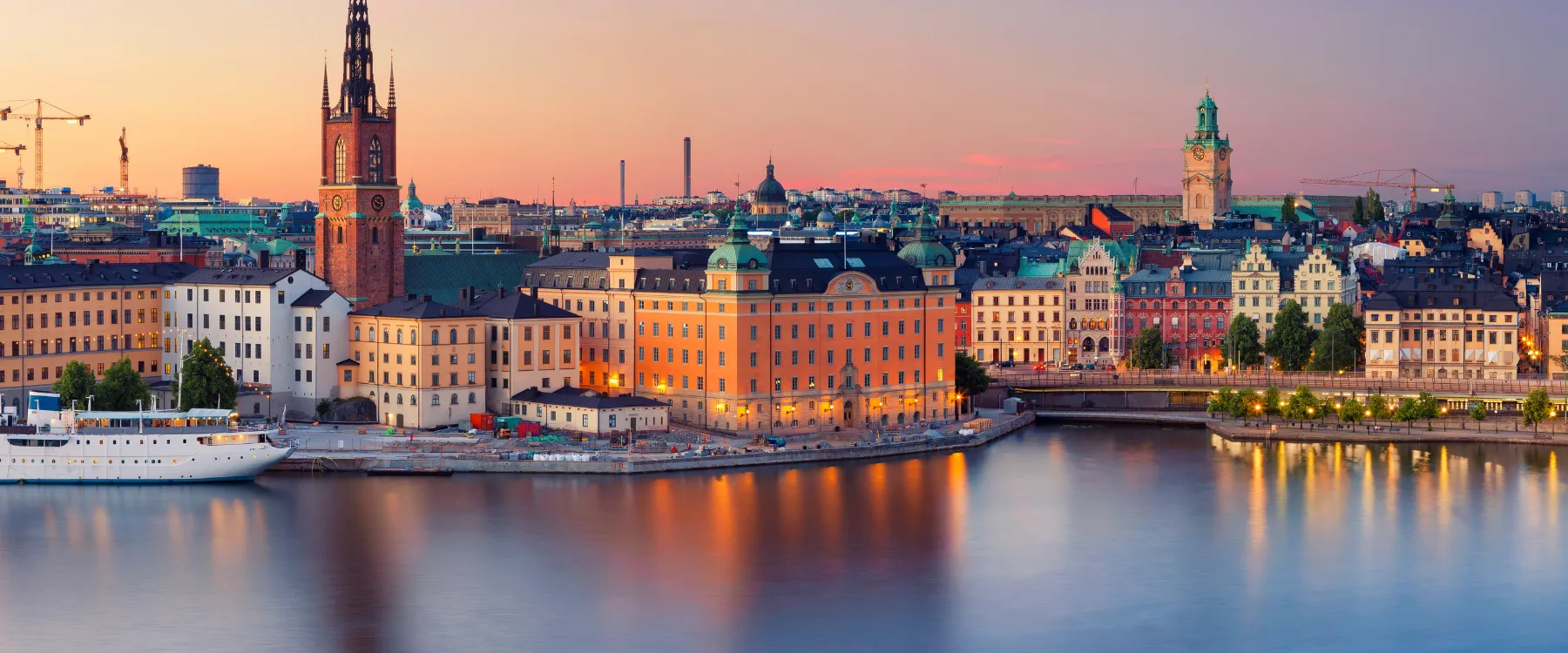 Gamla stan i Stockholm vid solnedgången med byggnader som speglar sig i vattnet.